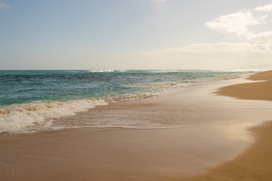 Beach and surf along Oahu's wild North Shore with waves breaking far from the shore.
