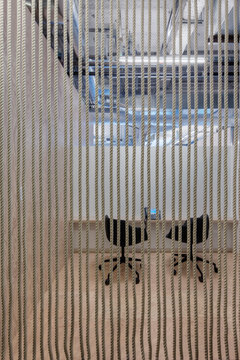 Two chairs in an office in a breakout area, view through a screen of vertical ropes.
