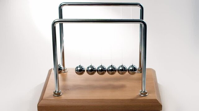 Slow-motion close-up of a Newton's cradle in action &ndash; seven chrome balls swinging in perfect rhythm, demonstrating momentum transfer in physics.