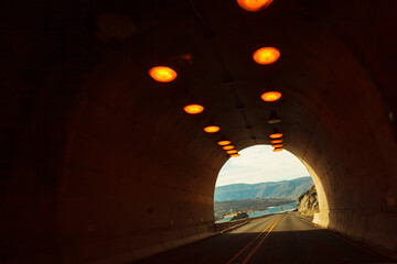 Two lane highway through a tunnel, view of the lights leading to the daylight and the end of the tunnel.