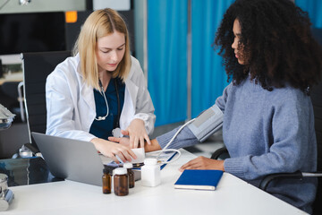 doctor checking woman blood pressure at clinic and filling patient history.