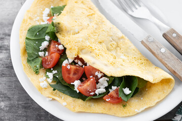 Stuffed omelette with tomatoes and spinach on wooden table