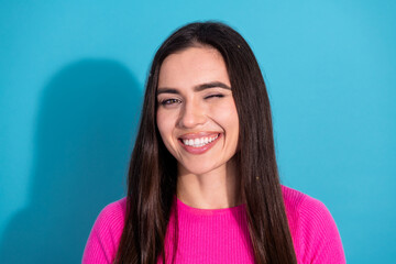 Cheerful young woman winking with a bright smile wearing a pink sweater, standing against a vibrant...