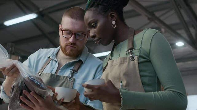 Low angle shot of female and male roasters working together, examining and discussing coffee beans at roasting plant