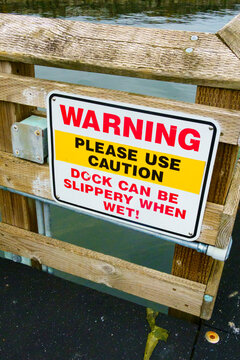 Warning sign on a wooden dock, red lettering, Please Use Caution, Deck can be slippery when wet.