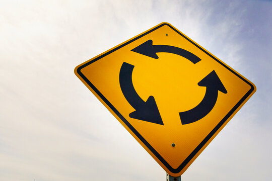 Round-a-bout traffic sign, yellow directional arrows, anticlockwise direction of flow, for a roundabout or circle road junction.