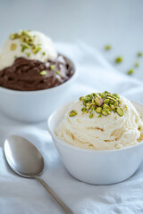 an inviting scene of fresh ice cream in white bowls, with one bowl featuring vanilla and another chocolate, topped with green pistachio nuts.