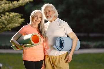 Obraz premium Senior couple with exercise mats standing at park and posing for a photo