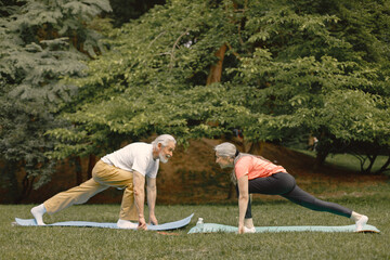 Senior couple standing at summer park and doing excercises on a yoga mats