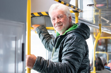 Portrait of bearded senior man dressed in winter clothes standing in bus during city commute
