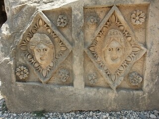 Stone slab with carved theatrical masks and floral elements from an ancient site, symbolizing art and drama