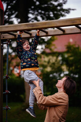 Obraz premium Parent Helping Child Hang on Monkey Bars at Playground