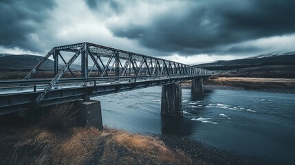 Obraz premium A weathered steel bridge stretching over a wide, slow-moving river under heavy clouds pic