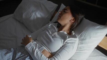 Woman sleeping in bed in a cozy home bedroom, captured indoors, highlighting her relaxed posture...