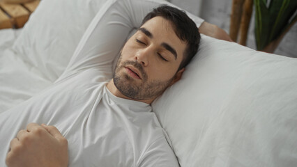 Handsome man sleeping peacefully on a comfy bed in a cozy bedroom setting inside a home, exuding a sense of relaxation and comfort in the indoor environment.
