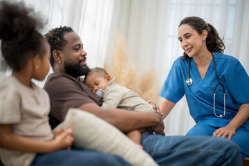 Caring doctor interacts with a father and his children at home during a wellness check in the...