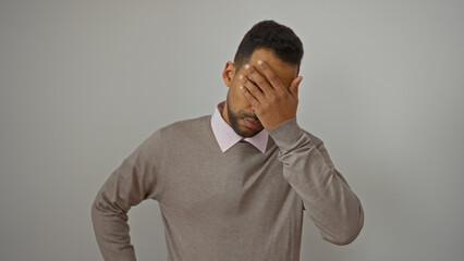 Young man with beard covering face with hand in frustration, wearing casual outfit, standing isolated over white background.