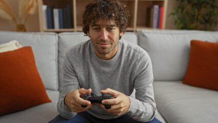 Young man playing video games on a comfortable sofa in a modern living room, focused on the screen,...