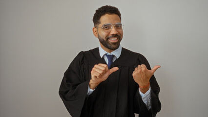 Happy graduate man in gown smiling and pointing to the side, standing against an isolated white background