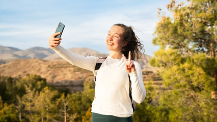A young hiker woman taking a selfie video in the mountains at sunrise. Tourist girl enjoying the...