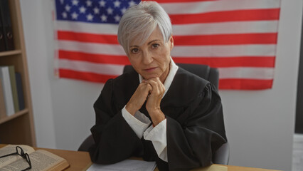 Mature woman judge with short grey hair in an office with an american flag background, wearing...