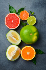 Different citrus fruits with leaves as background, top view