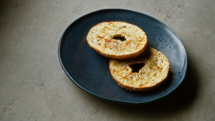 Two bagel halves on a blue plate placed on a concrete surface, showcasing a simple and delicious breakfast item.