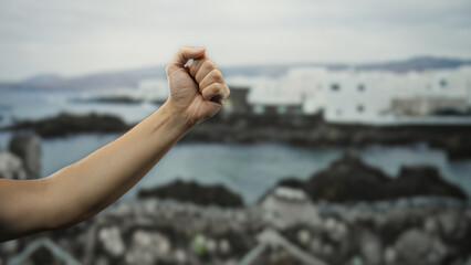 Man's hand clenched in a fist extends in front of a scenic seaside backdrop, capturing the essence...