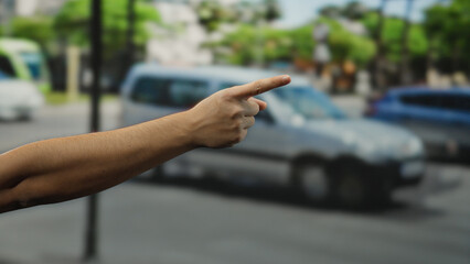 Man pointing hand on city street with cars in the background outdoors during daytime, indicating...