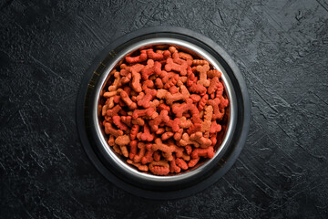 Dog food in a bowl. Organic grain food for dog on a black stone background. Top view.