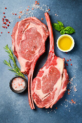 Two raw Tomahawk steaks, on the bone with rosemary, butter and salt. On a gray concrete background.