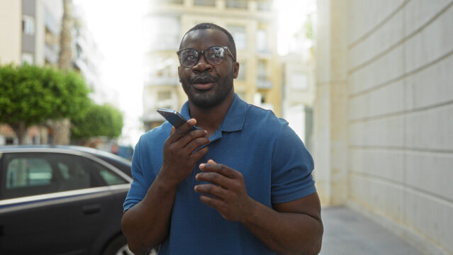 Young african american man in blue shirt talking on smartphone on urban street