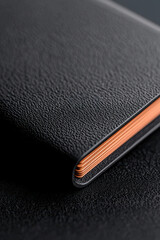 Close-up of black textured leather notebook with orange edges on dark background