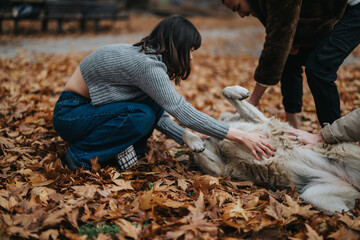 Obraz premium A heartwarming scene of two individuals enjoying a moment with a dog, creating joyful memories in the crisp autumn atmosphere.