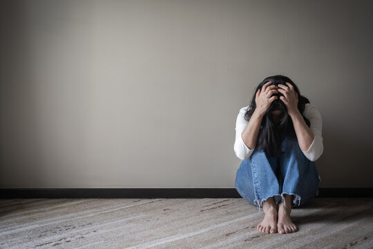 Panic attack woman, stressful depressed emotional person with anxiety disorder mental health illness, headache and migraine sitting feeling bad with back against wall on the floor in domestic home