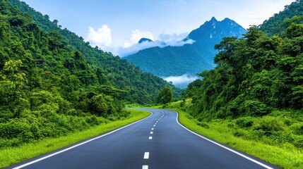 Fototapeta premium A winding road surrounded by lush greenery and mountains under a bright sky creates a serene landscape.