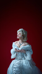 Naklejka premium Woman in historical gown rests hands on chest, gazing upward with expressive emotion on red backdrop. Concept of historical portrait, medieval times, character.