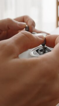 Vertical video. Person Holding and Plugging Cable into FPV Drone Joystick Controller near Laptop on Wooden Desk in Soft Daylight, Close-Up Side View, Manual Operation Concept