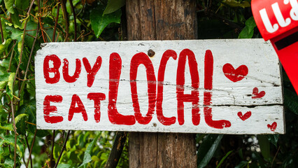 Hand-painted "Buy Eat Local" sign on a wooden post in rural Thailand