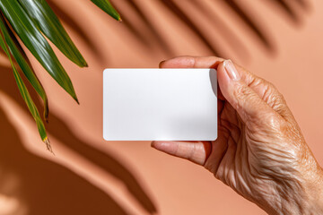 Elderly caucasian female hand holding blank card on brown background with leaf shadow