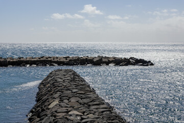 Black stone piers in the Atlantic Ocean with reflected sunlight and glare