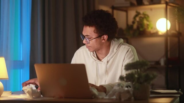 Stressed young man holding head in frustration while nervously speaking on phone and looking at laptop dealing with overwhelming situation mistake or urgent problem late at night at home