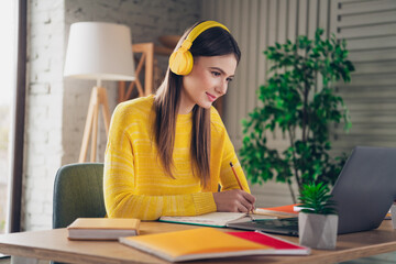 Woman Studying at Home Wearing Yellow Headphones and Sweater Using a Laptop While Smiling and...