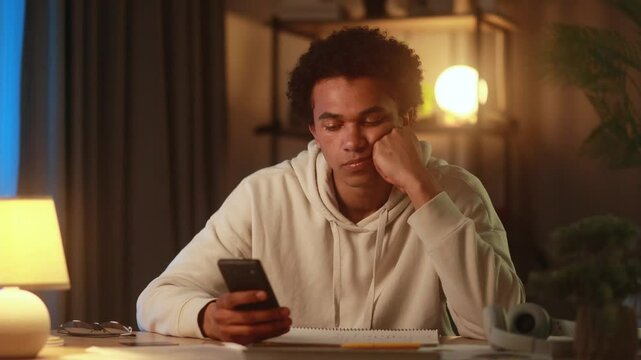 Young man browsing online store on smartphone at night suddenly finds something amazing and excitedly grabs his bank card to make a quick purchase surprised and delighted after long search