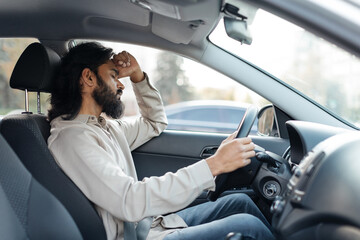 Indian man in car showing frustration or fatigue, eyes closed, tired eastern male resting head on...