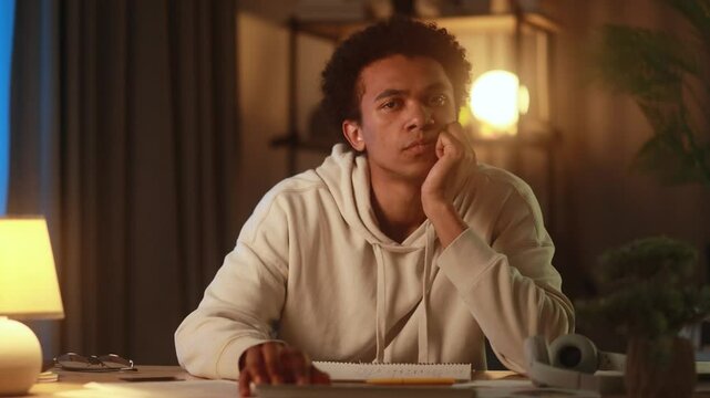 Camera view of young african american man at desk browsing online store and struggling to find something he likes looking unimpressed and indecisive while shopping on laptop at home in the evening