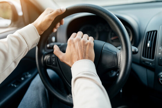 Closeup of young man honking while driving, sitting in car. Selective focus on steering wheel, unrecognizable driver beeping the horn in auto. Transportation and traffic concept