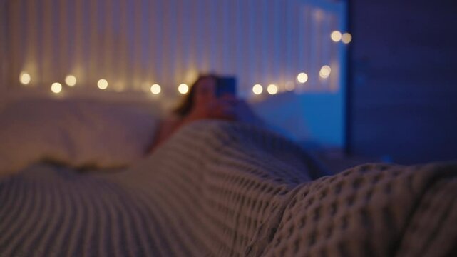 Camera Rising From Under Bed Gliding From Woman&rsquo;s Feet to Face While She Lies Under Blanket Using Smartphone, Warm Lights and Blue Hue, Tracking Shot, Night Scrolling Concept