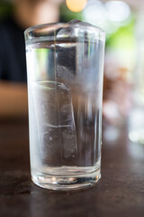 Close up a glass of fresh water with ice cubes on the wooden table ready to drink at dinner meal time, drinking water at dinner meal time at restaurant