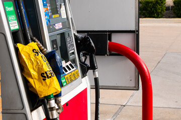 A side view of a mainly red gas pump. One of the gas nozzles is listed as out of service while the...